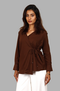 Woman wearing a fullblank branded brown shirt called COCO-A with a plain background