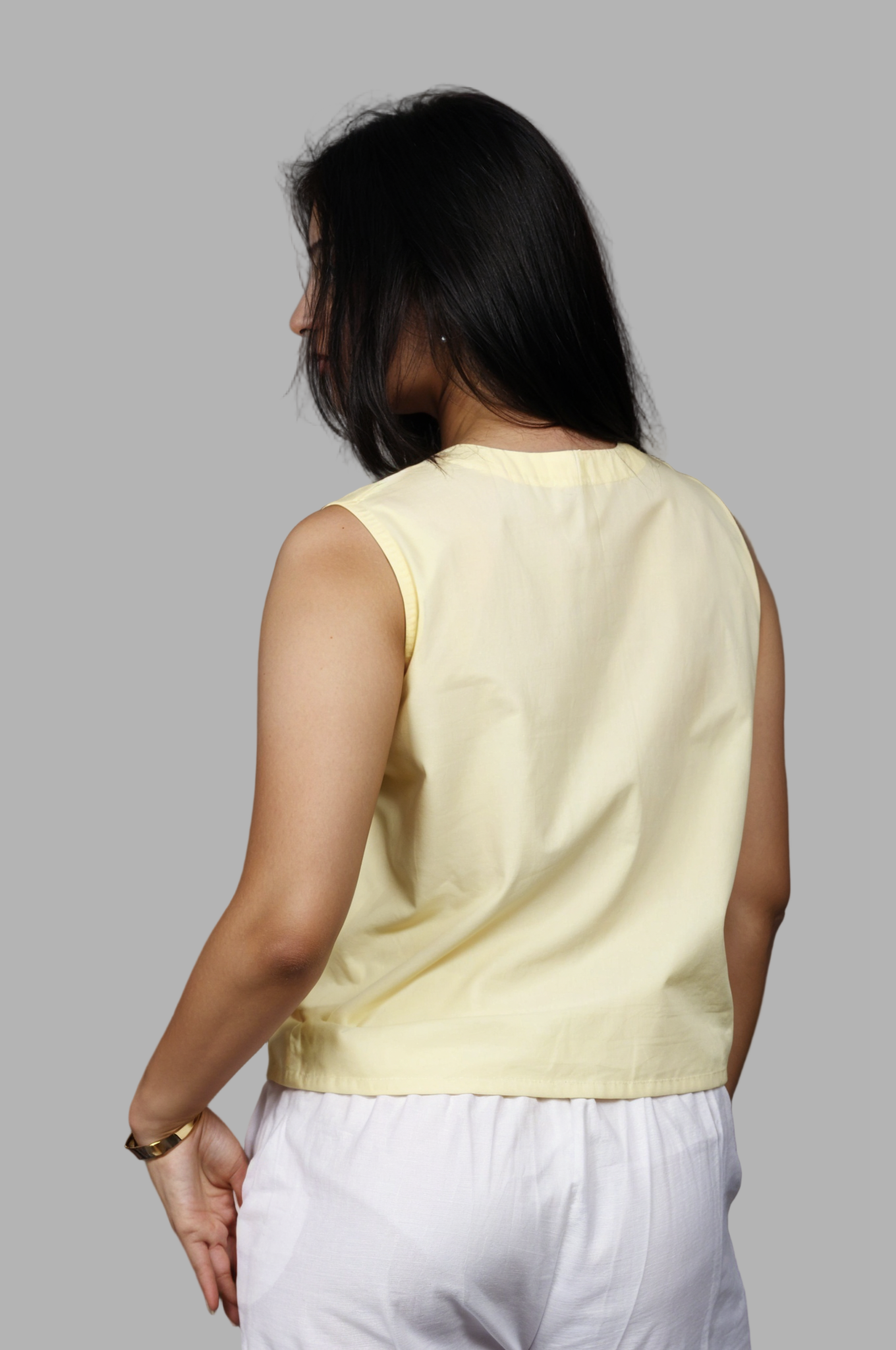 Woman wearing a fullblank branded light yellow sleeveless top called KIKI-B with a plain background